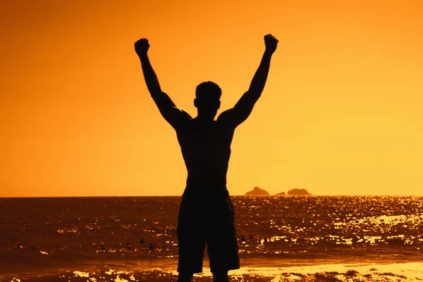 一个欢呼运动的人的剪影在室外日落在海滩作为冠军的标志 — 图库照片