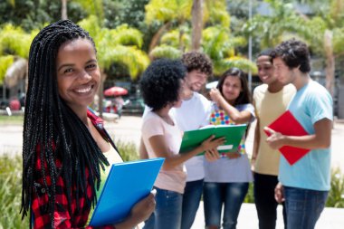 Laughing african female student with group of students outdoor on campus of university in summer clipart