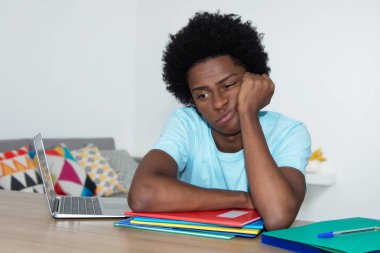 Unmotivated african american male student at desk at home at desk clipart