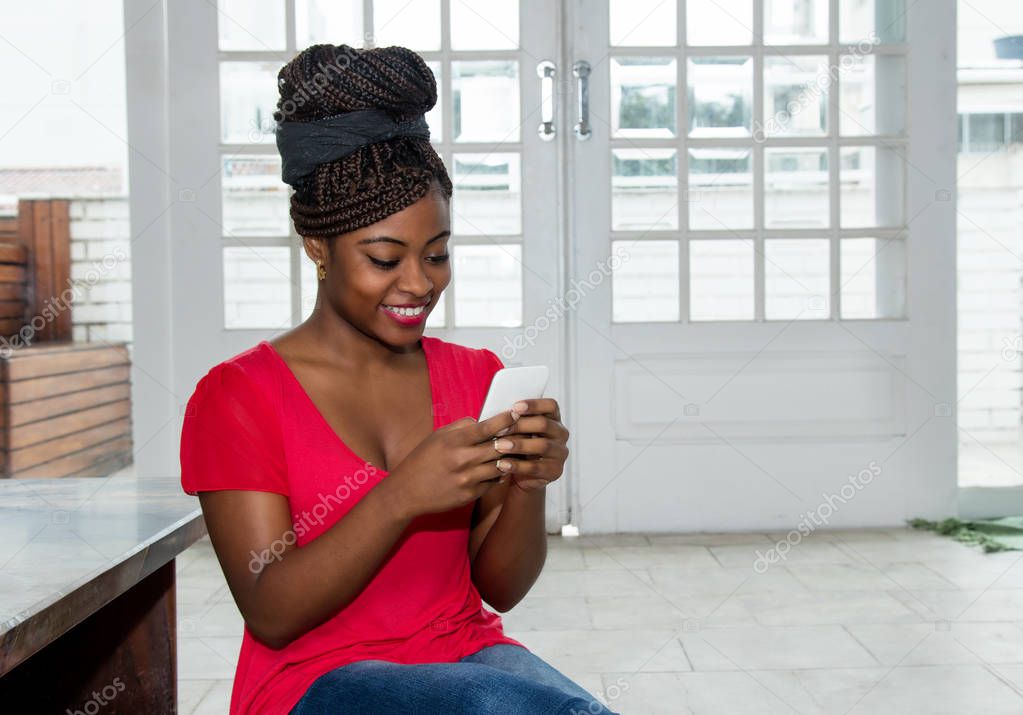 Beautiful african american woman sending message with phone at home