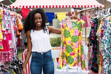 Beautiful african american woman selling clothes to customers at typical market clipart