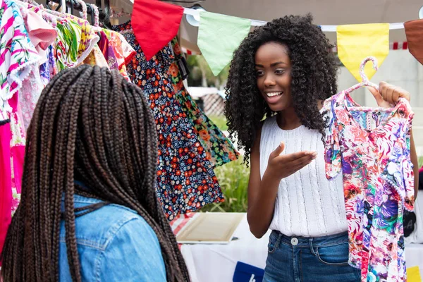 美しいアフリカ系アメリカ人市場ベンダーのカラフルな服を典型的な市場で顧客に提示 — ストック写真