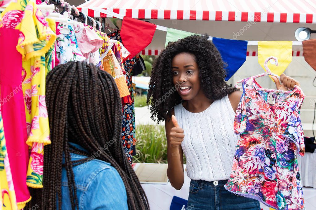 African american woman showing colorful clothes to buyer at typical market