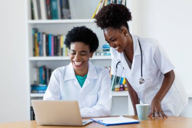 Genç hemşire ile Afrikalı-Amerikalı kadın Doktor hastanede gülüyor