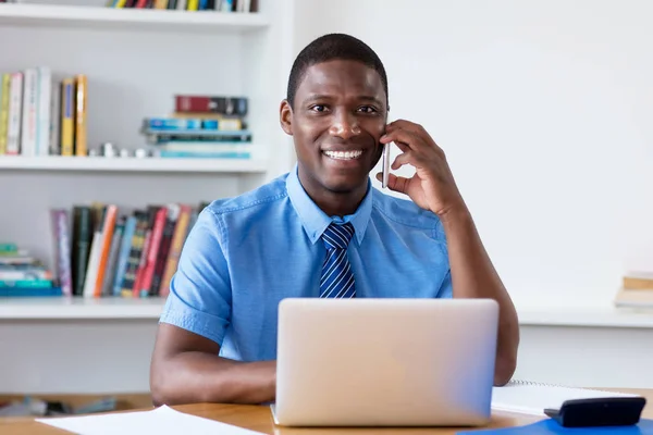 Laughing african american businessman with necktie at mobile phone at office
