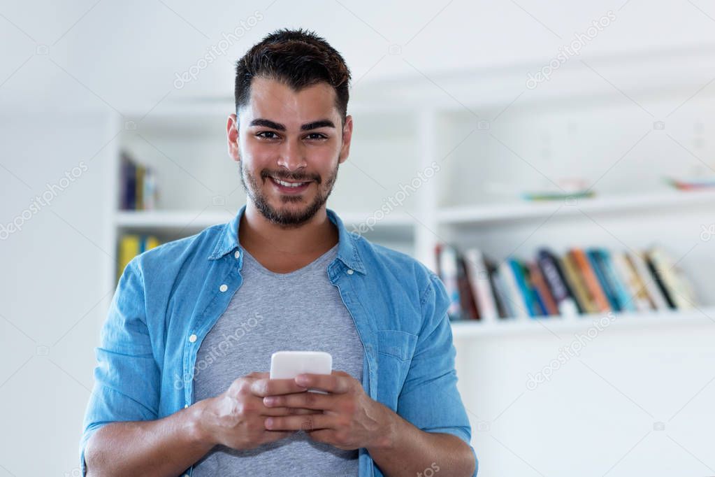 Mexican hipster man with beard sending message with phone indoor at home