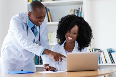 Afro-Amerikan erkek doktor ve hemşire Hastanesi'nde bilgisayar başında çalışırken gülüyor