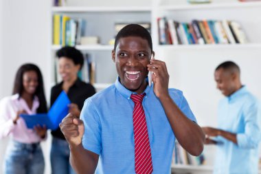 Şirket ofisindeki meslektaşları ile telefon, kravat ile Afrika kökenli Amerikalı işadamı tezahürat
