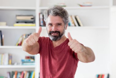 Her iki başparmak kapalı evde gösterilen gri saçlı yakışıklı Alman orta yaşlı adam