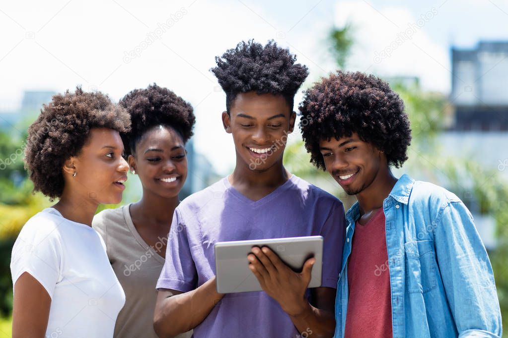 Group of african american young adults posting message with digital tablet outdoor in the summer
