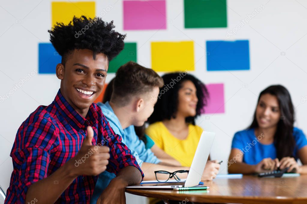 Laughing african american male student at computer with group of