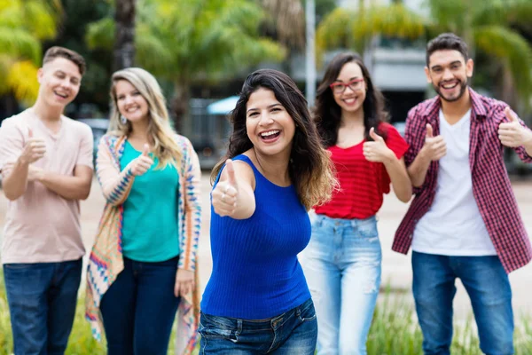 Risate messicana donna mostrando entrambi i pollici con gruppo di youn — Foto Stock