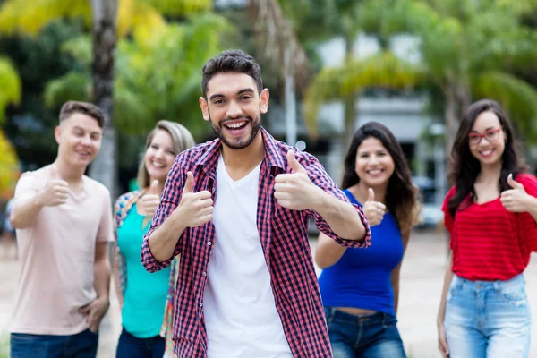 Hipster giovane adulto con barba mostrando pollice in su con gruppo di fr — Foto Stock