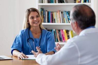 Gülen sarışın hemşire doktorla konuşuyor.