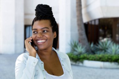 Afrikalı Amerikalı genç yetişkin bir kadın telefona gülüyor.