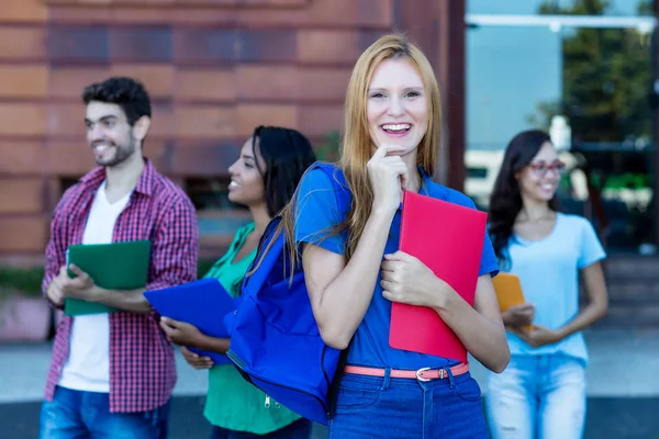 Estudante muito feminino com cabelos vermelhos e grupo de jovens adultos — Fotografia de Stock