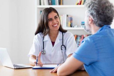 Gülen Meksikalı kadın doktor hastayla hastanede konuşuyor.