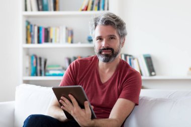 Alman yetişkin bir adam evdeki tablet bilgisayarında haber ve e-kitap okuyor.