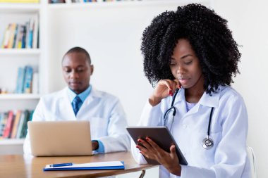 Afro-Amerikan tıp öğrencisi dijital tablet bilgisayarında erkek bilim adamıyla hastanede.
