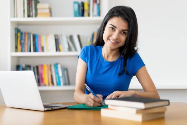Laughing turkish female student at desk at home or at library clipart