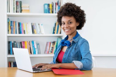 Gülen Afrikalı Amerikalı genç yetişkin kadın evdeki masada bilgisayarın başında.