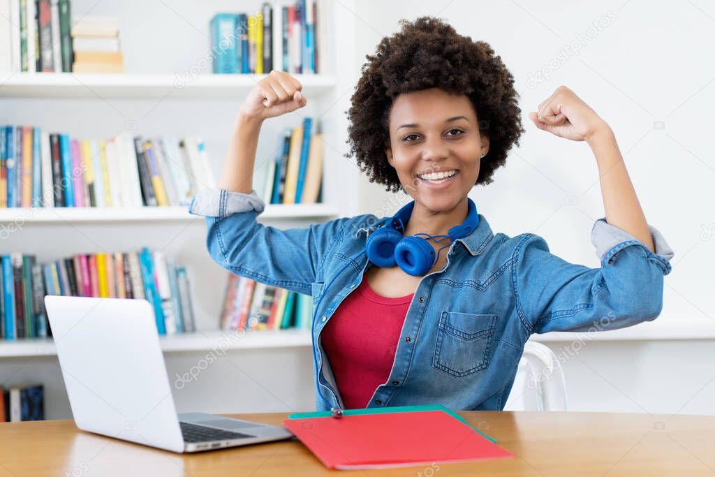 Cheering african american young adult woman at computer indoors at desk at home