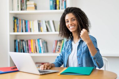 Evde bilgisayar başında kıvırcık saçlı başarılı Latin kız öğrenci.