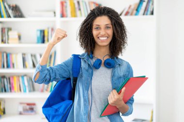 Üniversite sınıfında kıvırcık saçlı ve evrak işleriyle tezahürat yapan Latin kız öğrenci.