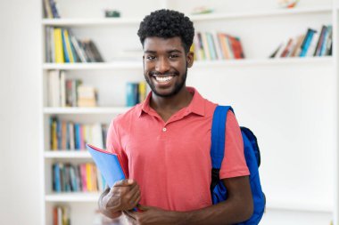 Üniversite kütüphanesinde sırt çantalı Afro-Amerikan erkek öğrencinin portresi