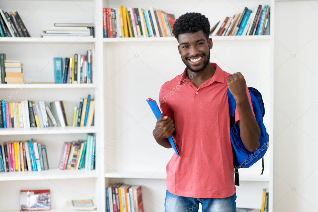 Cheering afro american male student with backpack and copy space at library of university
