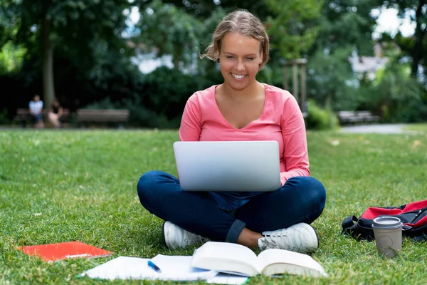 Beautiful german female student at computer learning and preparing for degree outdoor in park on campus of university