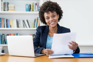 Kahkahalar atan Afro-Amerikan iş adamı ofis masasında çalışıyor.