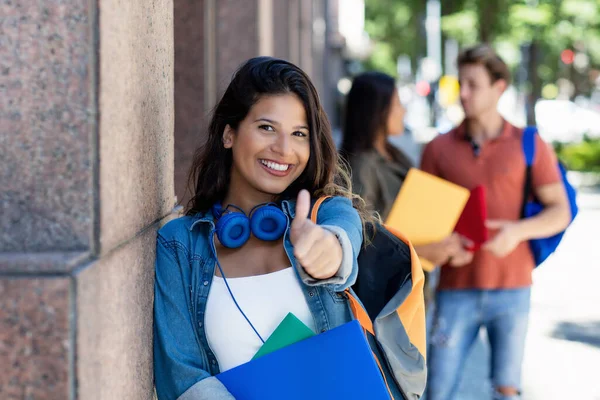 成功した笑いの女性学生は 都市で夏に屋外大学の建物の前に背景に友人と親指を表示します — ストック写真