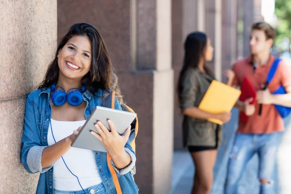 Pretty female student with tablet computer and friends in background in front of university building outdoor in summer in city
