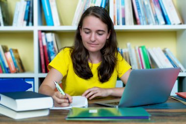 Güzel Alman kız öğrenci evde masa başında kitap ve bilgisayarla öğreniyor.