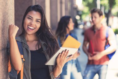 Dijital tablet bilgisayarlı Latin Amerikalı bayan öğrenci ve diğer genç yetişkinler üniversite binasının önünde tezahürat yapıyor.