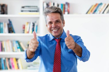 Kravat takmış gülen iş adamı iş yerinde iki parmağını da gösteriyor.