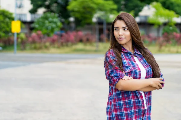 Uzun siyah saçlı ve yazın açık havada fotokopi çeken kendine güvenen Latin Amerikalı genç bir yetişkin kadın.