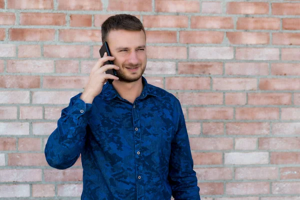 Handsome british man with stubble talking with girlfriend at phone in front of brickstone wall in England