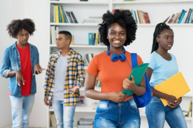 Üniversitenin kütüphanesinde Afro-Amerikan genç yetişkinler grubuyla birlikte gülen siyah kız öğrenci.
