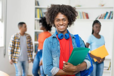 Üniversitenin kütüphanesinde Afro-Amerikalı genç yetişkinlerle birlikte gülen siyah erkek öğrenci.