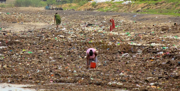 海の汚染 スリランカのビーチの海からの波によってもたらされたゴミの山の中で女性がプラスチックのものを収集します — ストック写真