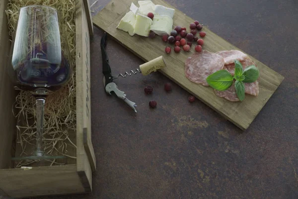 Rotweinglas mit Käse und Salami in Holzkiste auf Betontisch — Stockfoto