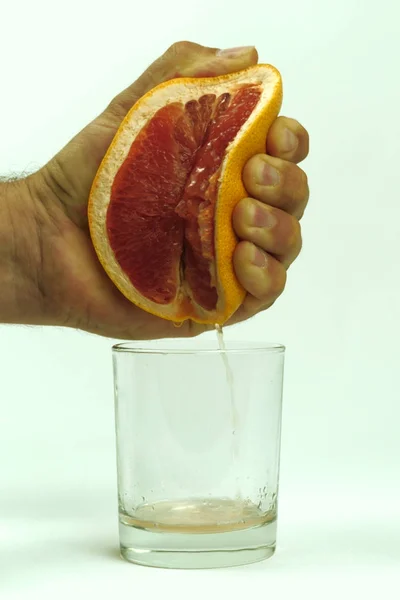 Homem espremendo metade da toranja suculenta para vidro vazio no fundo branco, close-up — Fotografia de Stock