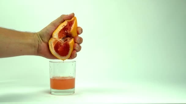 Mann drückt die Hälfte der saftigen Grapefruit auf leeres Glas auf weißem Hintergrund, Nahaufnahme — Stockvideo