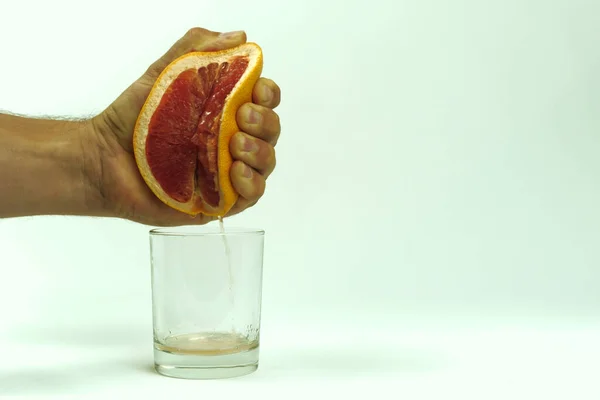 Man squeezing half of juicy grapefruit to empty glass on white background, close up — Stock Photo, Image