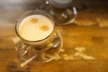 Glass mug with coffee latte in coffee on a vintage wooden table. Photo in dim light in warm colors on a wooden table, lifestyle photo clipart