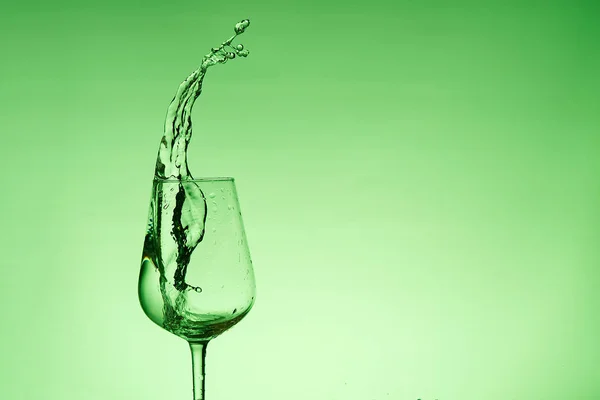 Krásné cákance vody ve sklenici vína, se zeleným filtrem, zblízka s kopírovacím prostorem. — Stock fotografie