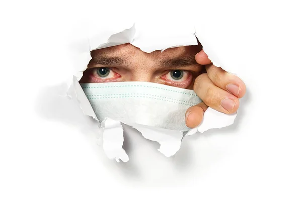 Man in medical mask peeping through hole on paper. Male Eye looking through hole. Isolated on white background. covid - 19 concept, coronavirus — Stock Photo, Image