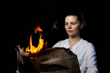 A woman is holding a burning newspaper. Fake news concept. clipart